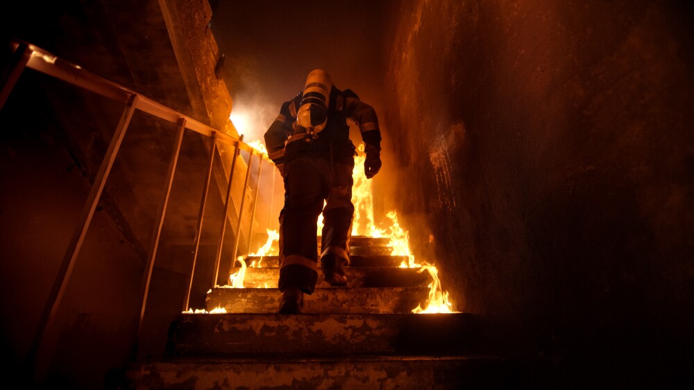 Strong and brave Firefighter Going Up The Stairs in Burning Building. Stairs Burn With Open Flames.